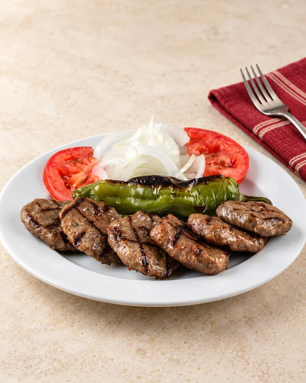 Beyaz tabakta ızgara köfte, közlenmiş biber, domates ve soğan